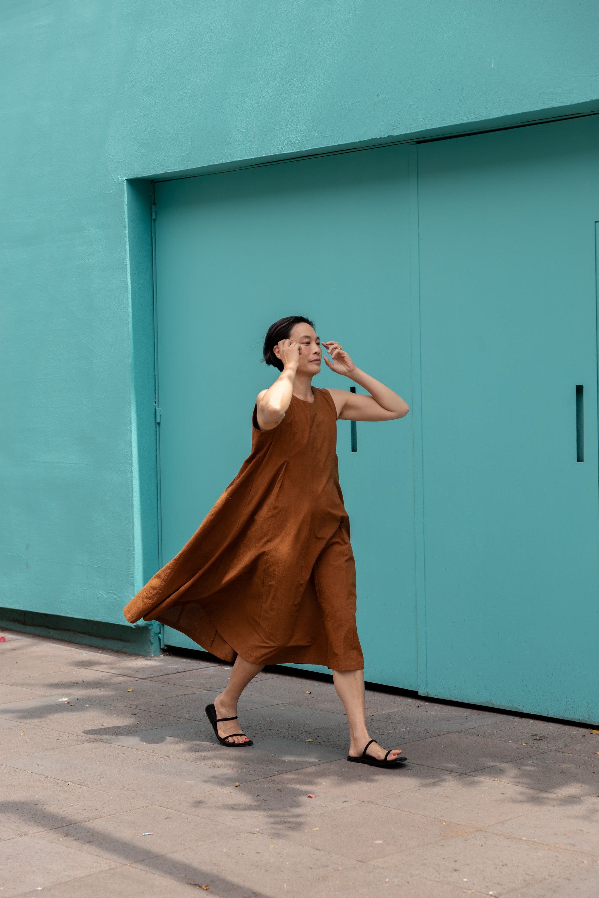 Sleeveless caramel-brown A-line midi dress with a high, round neckline. Features a voluminous flared silhouette, creating a breezy and effortless look. Made from textured, lightweight fabric for a natural, flowy drape.