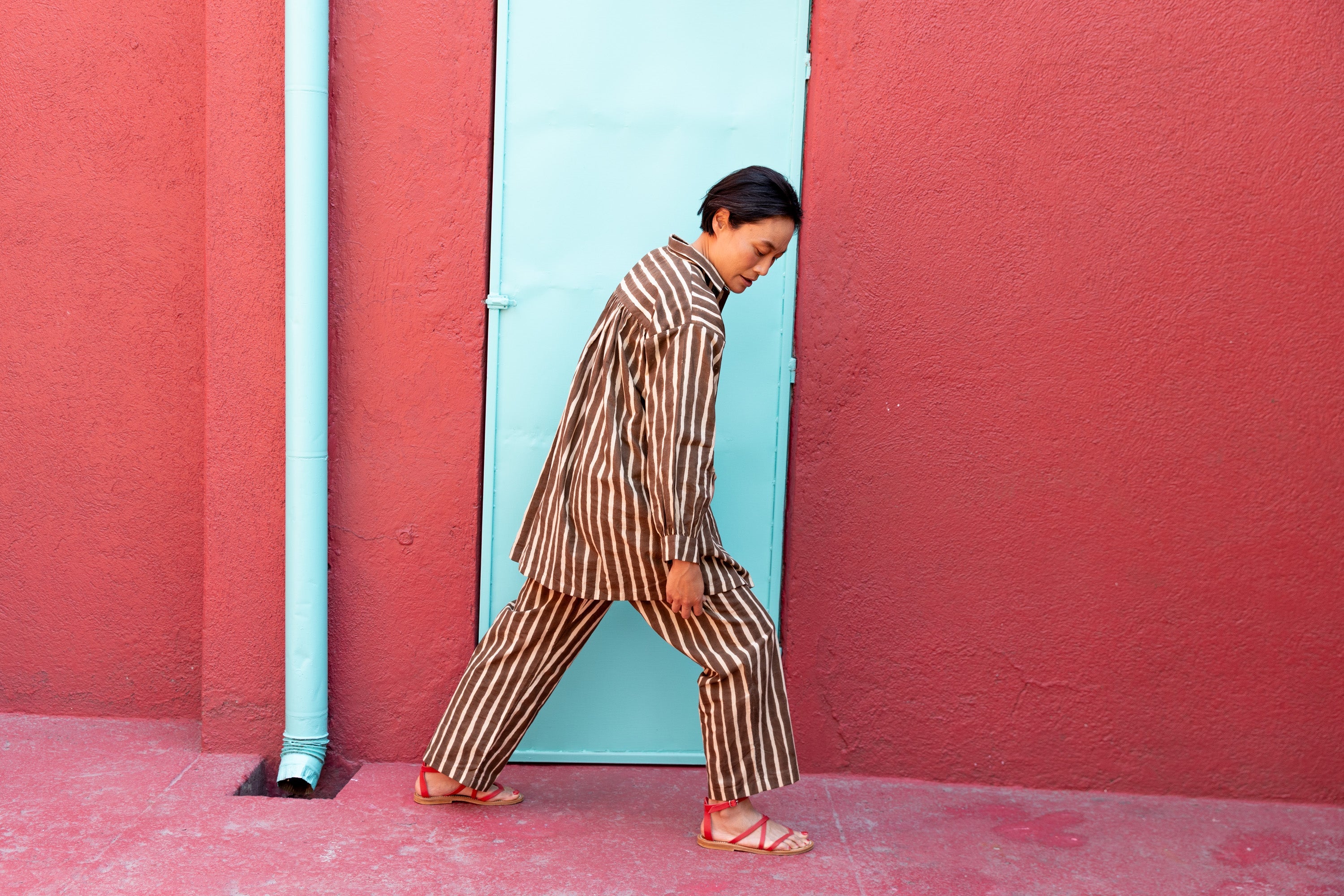 Brown and white vertically striped wide-leg pants with a relaxed, flowy fit. The high-waisted design offers a comfortable and effortless silhouette. The lightweight fabric drapes naturally, making the pants ideal for casual or lounge wear. The bold stripe pattern elongates the legs, adding a stylish touch to the relaxed aesthetic.