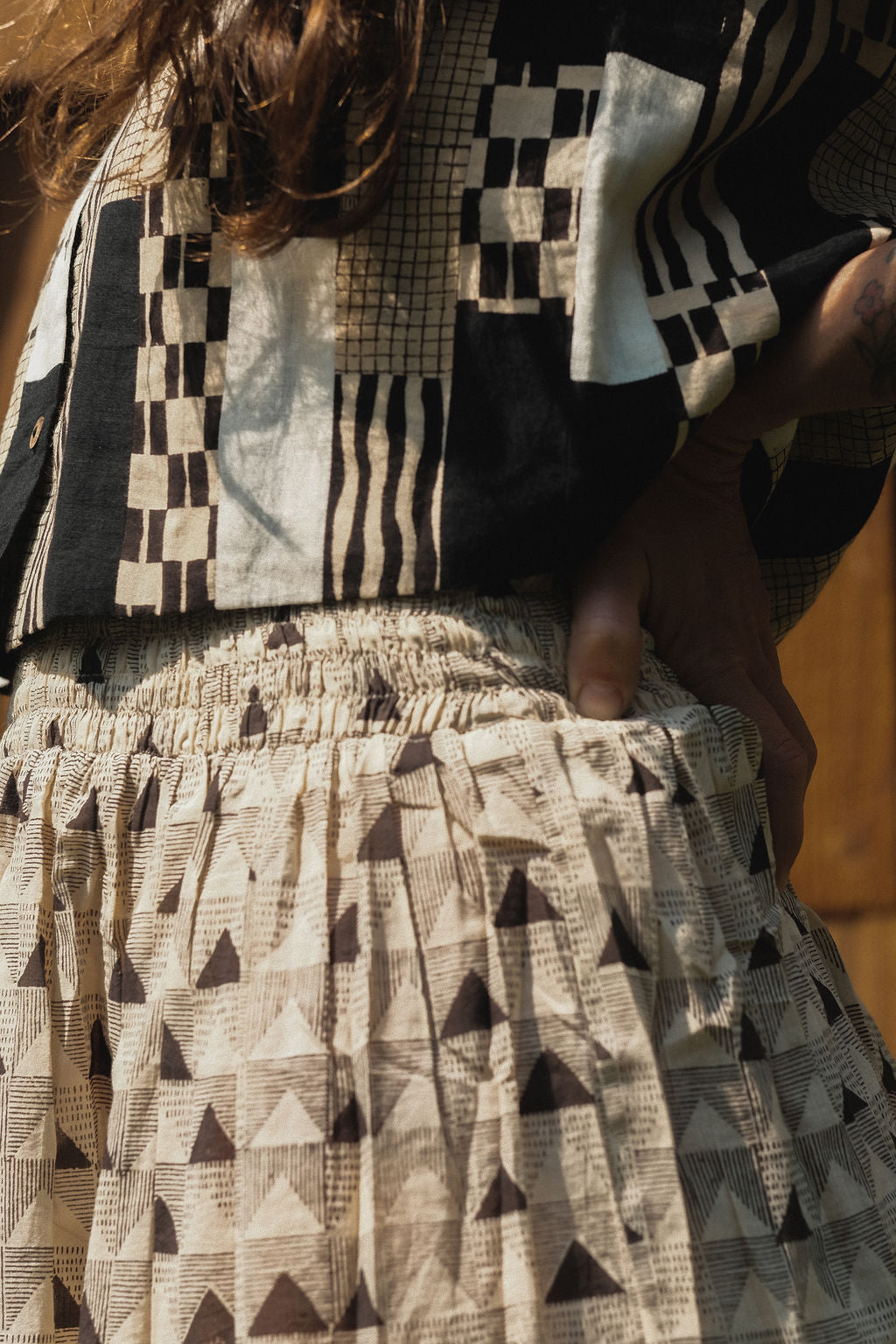 A mid-length, handwoven skirt made from soft, breathable organic cotton. The fabric features a delicate, all-over triangular block print in muted tones of black and grey on an off-white base. Lightly gathered at the waist, the skirt flows into a relaxed, voluminous silhouette that offers both comfort and movement. Naturally dyed and finished with a subtle texture, the skirt has an earthy, artisanal feel ideal for everyday wear.