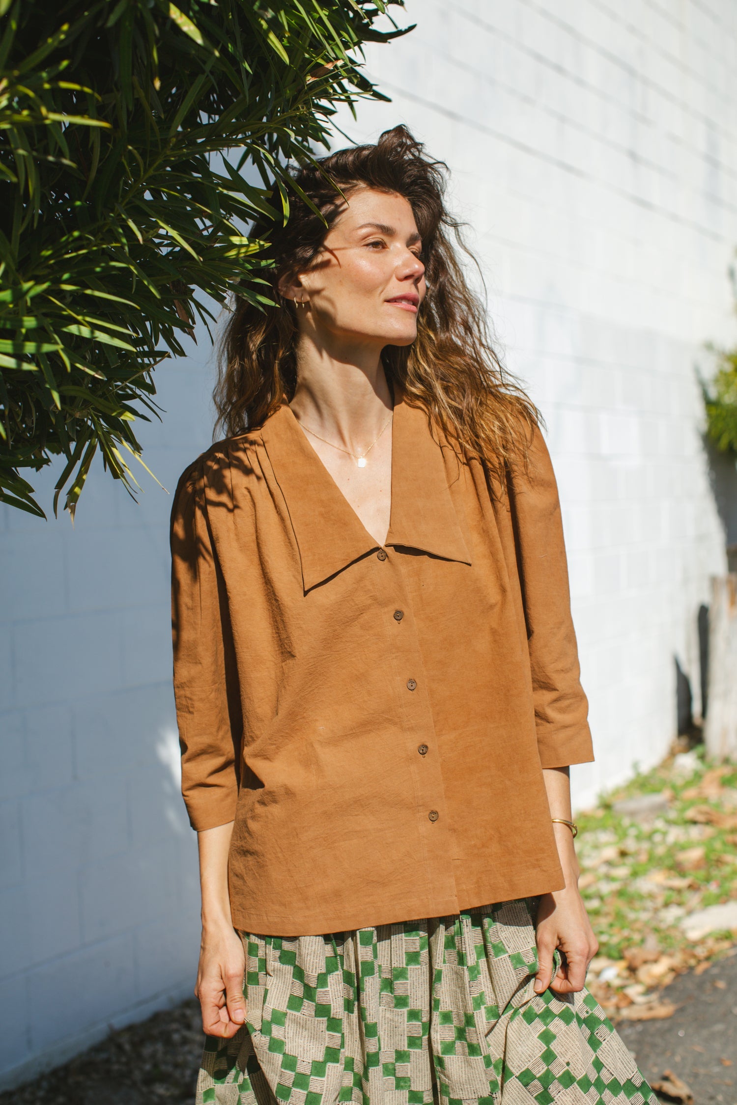 Vintage-inspired brown suede blouse with a wide-notch collar and gathered shoulders, adding a touch of retro elegance. The earthy caramel hue enhances its timeless appeal, making it a versatile statement piece.