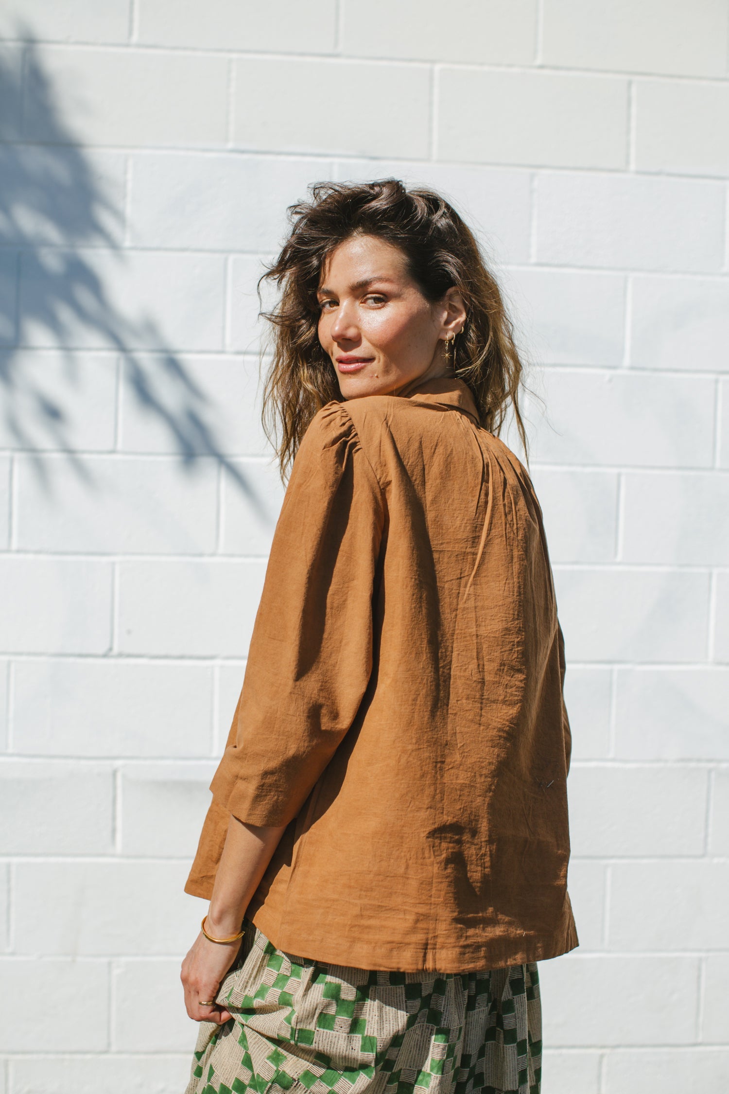 Vintage-inspired brown suede blouse with a wide-notch collar and gathered shoulders, adding a touch of retro elegance. The earthy caramel hue enhances its timeless appeal, making it a versatile statement piece.