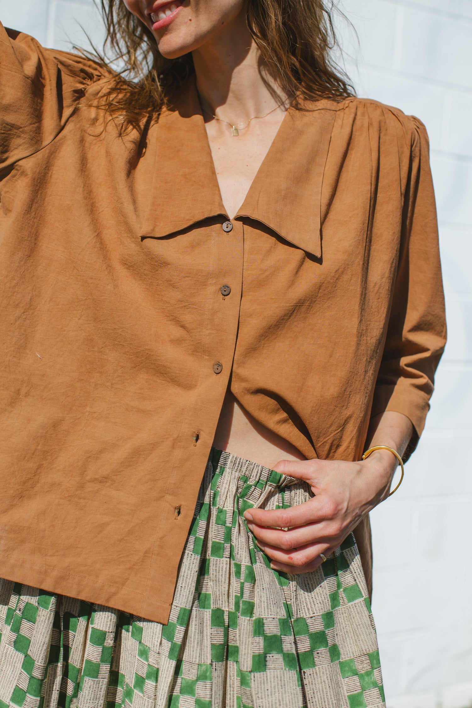 Vintage-inspired brown suede blouse with a wide-notch collar and gathered shoulders, adding a touch of retro elegance. The earthy caramel hue enhances its timeless appeal, making it a versatile statement piece.