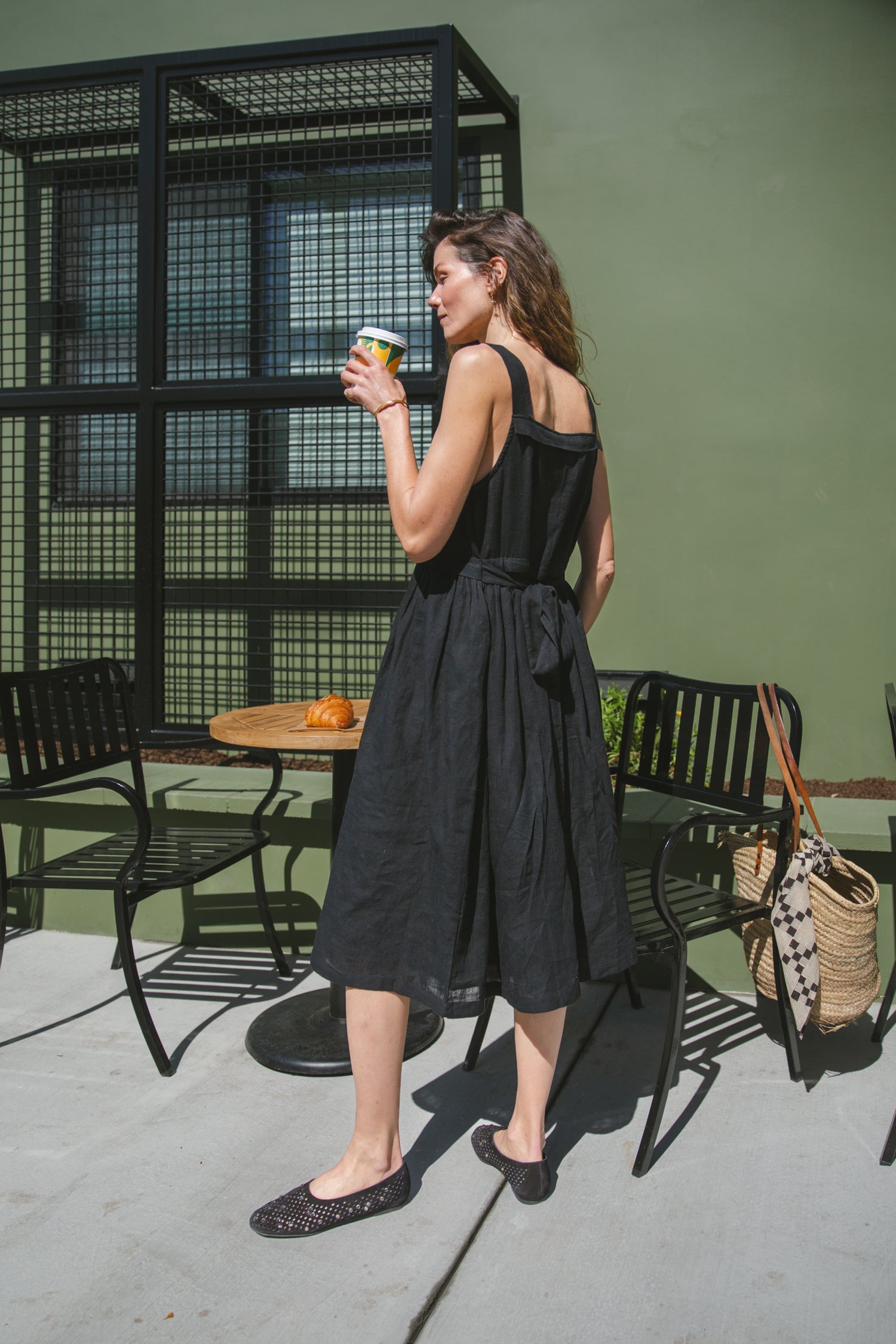 This is a black sleeveless midi dress with a structured square neckline and wide shoulder straps. The dress features a loose, flowing silhouette with a gathered waistline that adds volume and movement. Crafted from a lightweight, breathable fabric, it drapes effortlessly, making it perfect for warm weather. Functional side pockets enhance its practicality, while the relaxed fit exudes a laid-back yet refined charm. The minimalist design and deep black hue create a versatile piece that can be styled casually