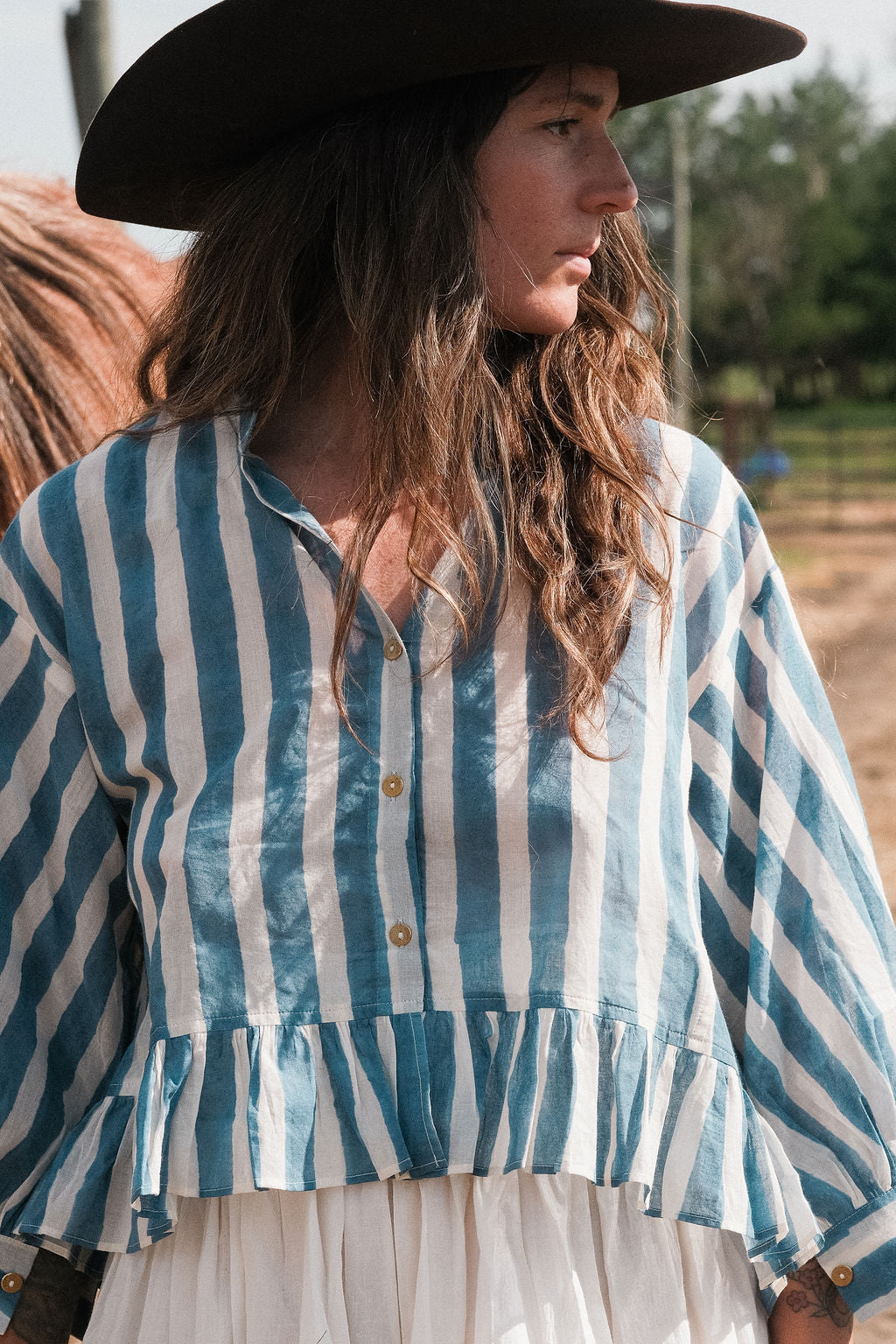Handwoven blue and white striped cotton top featuring a V-neckline, button-down front, and gathered peplum hem. Made from breathable organic cotton with natural dyes, this lightweight blouse offers a relaxed fit with full sleeves—perfect for summer and resort wear.