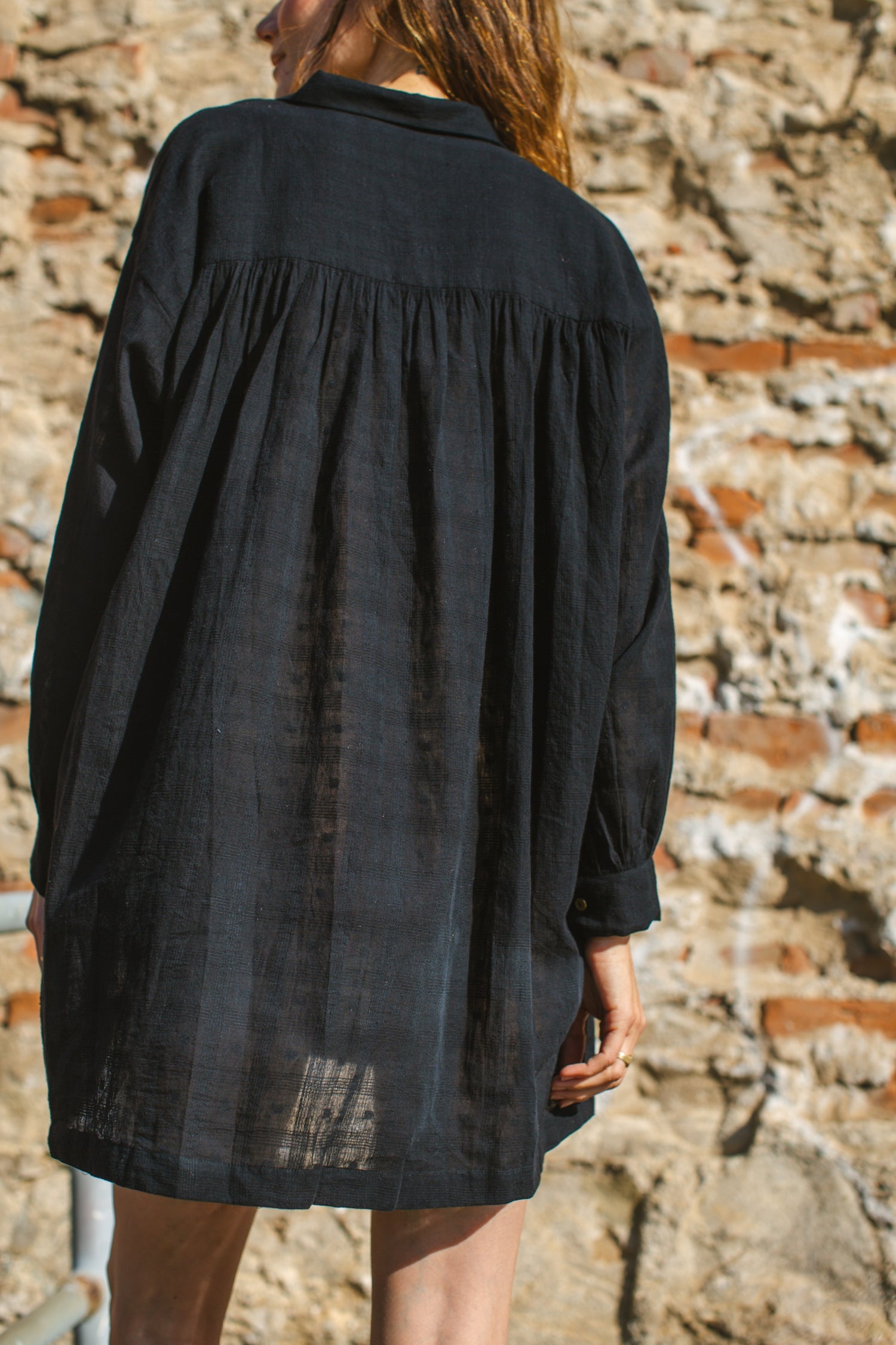 Black artist smock with a relaxed, oversized fit, featuring a button-down front, billowy long sleeves with gathered cuffs, and a subtle textured fabric. The lightweight, breathable material drapes effortlessly, creating a casual yet artistic look.