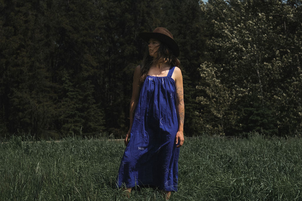 Long indigo blue Jamdani dress featuring wide straps, a gathered neckline, and subtle white abstract geometric motifs. Handwoven from soft, lightweight cotton and dyed with azo-free dyes, this fully lined dress is crafted over 7 days using traditional weaving techniques. Ethically made with a relaxed, bohemian silhouette, it's perfect for summer wear—combining artisanal charm with breathable comfort.