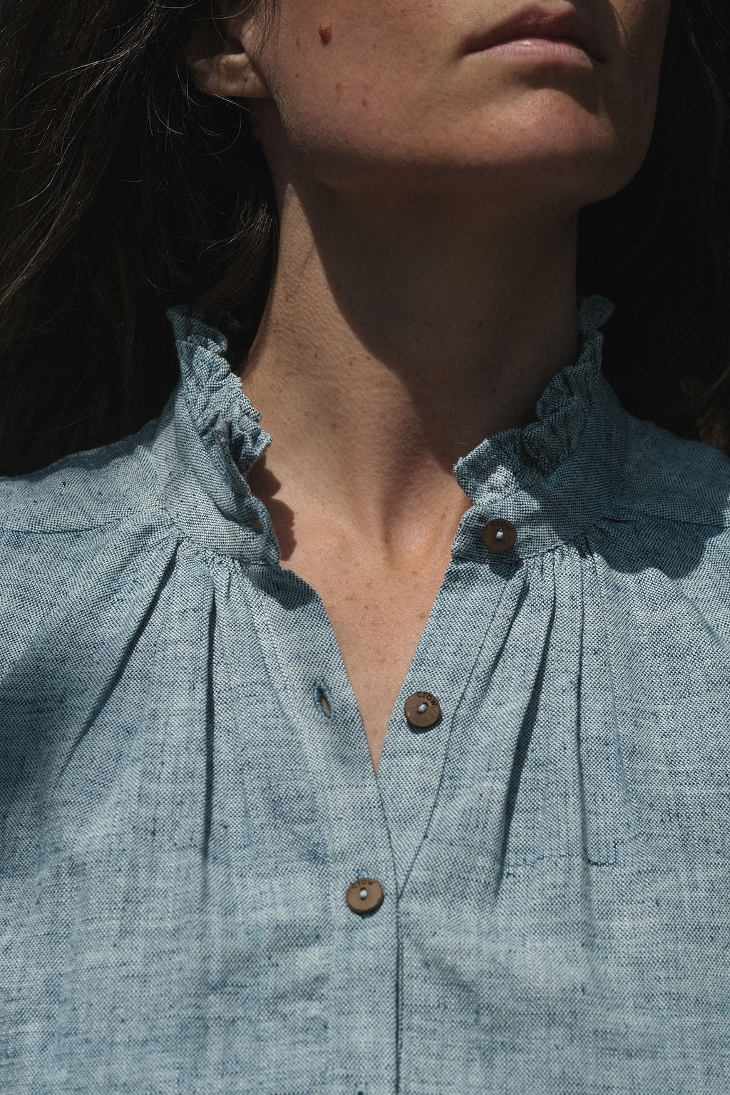 Sleeveless chambray blue top made from soft, handwoven organic cotton. Features a short button placket at the front and a subtle pleat detail below the collar, creating a clean and structured look. The stand collar adds a modern touch, while the breathable, lightweight fabric ensures comfort in warmer weather. Naturally dyed and ethically crafted, this top is perfect for effortless, everyday wear.