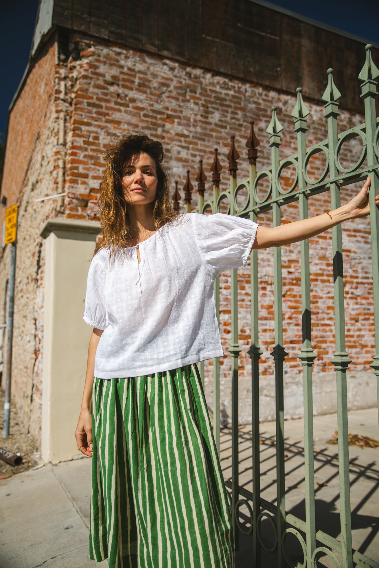 Lightweight white cotton top with a subtle textured weave, featuring a relaxed fit and airy design. The blouse has a gathered scoop neckline with delicate tie details, adding a touch of softness. Puff sleeves with gentle pleats create volume, while the slightly cropped hem gives it a modern, effortless feel.