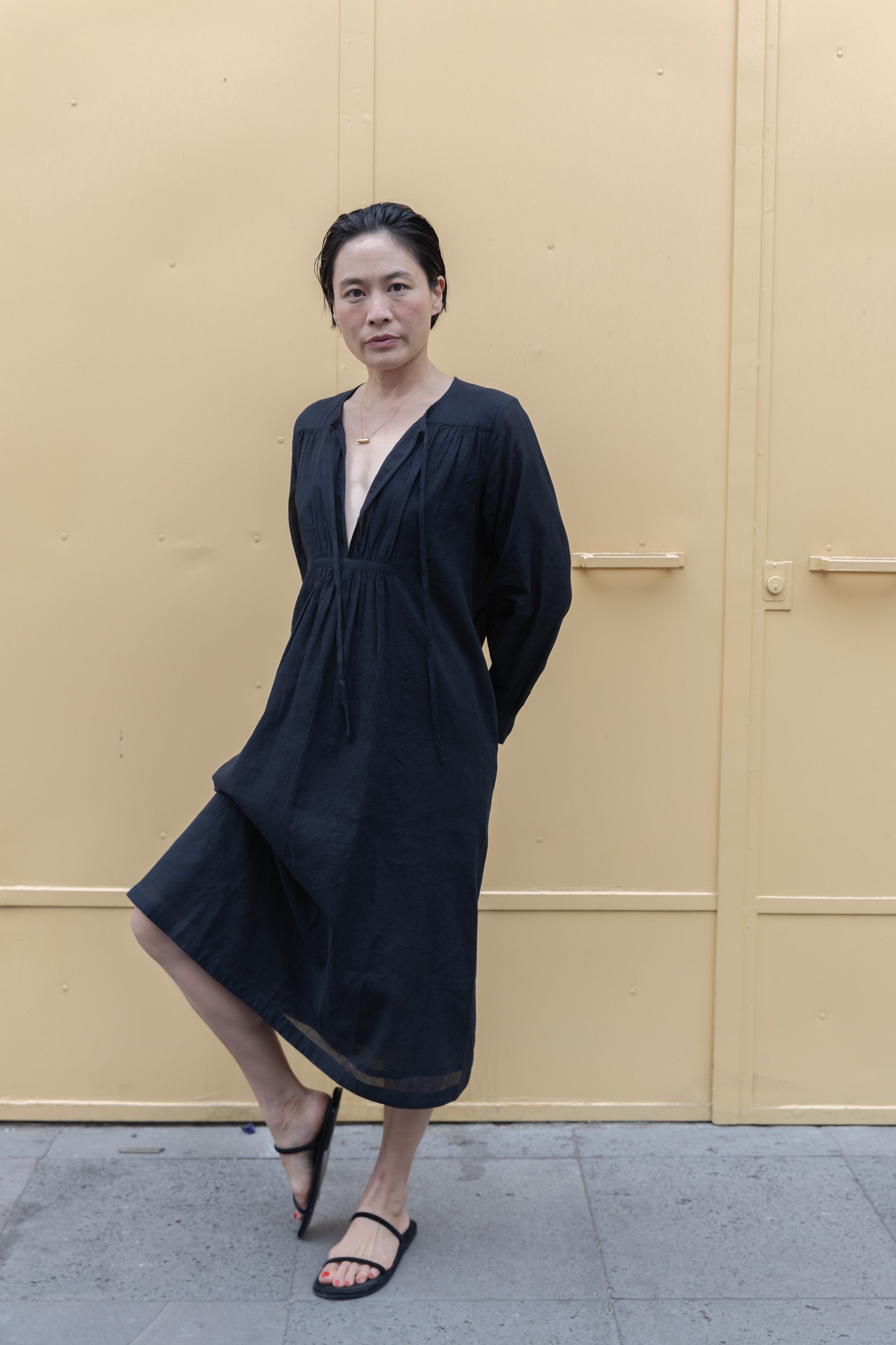 Black midi dress with long sleeves, a deep V-neckline with delicate gathers, and adjustable tie details. Designed with a relaxed waist and flowy fabric for effortless movement.