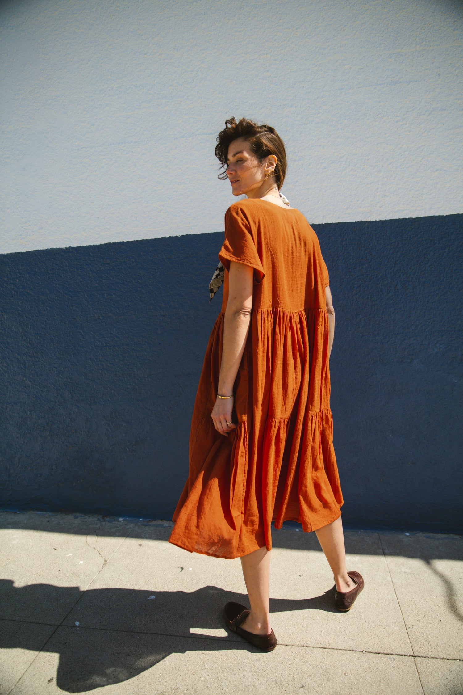 Rust orange tiered midi dress with a relaxed fit, short sleeves, a round neckline with a buttoned placket, and soft, lightweight fabric for an effortless, breezy style.