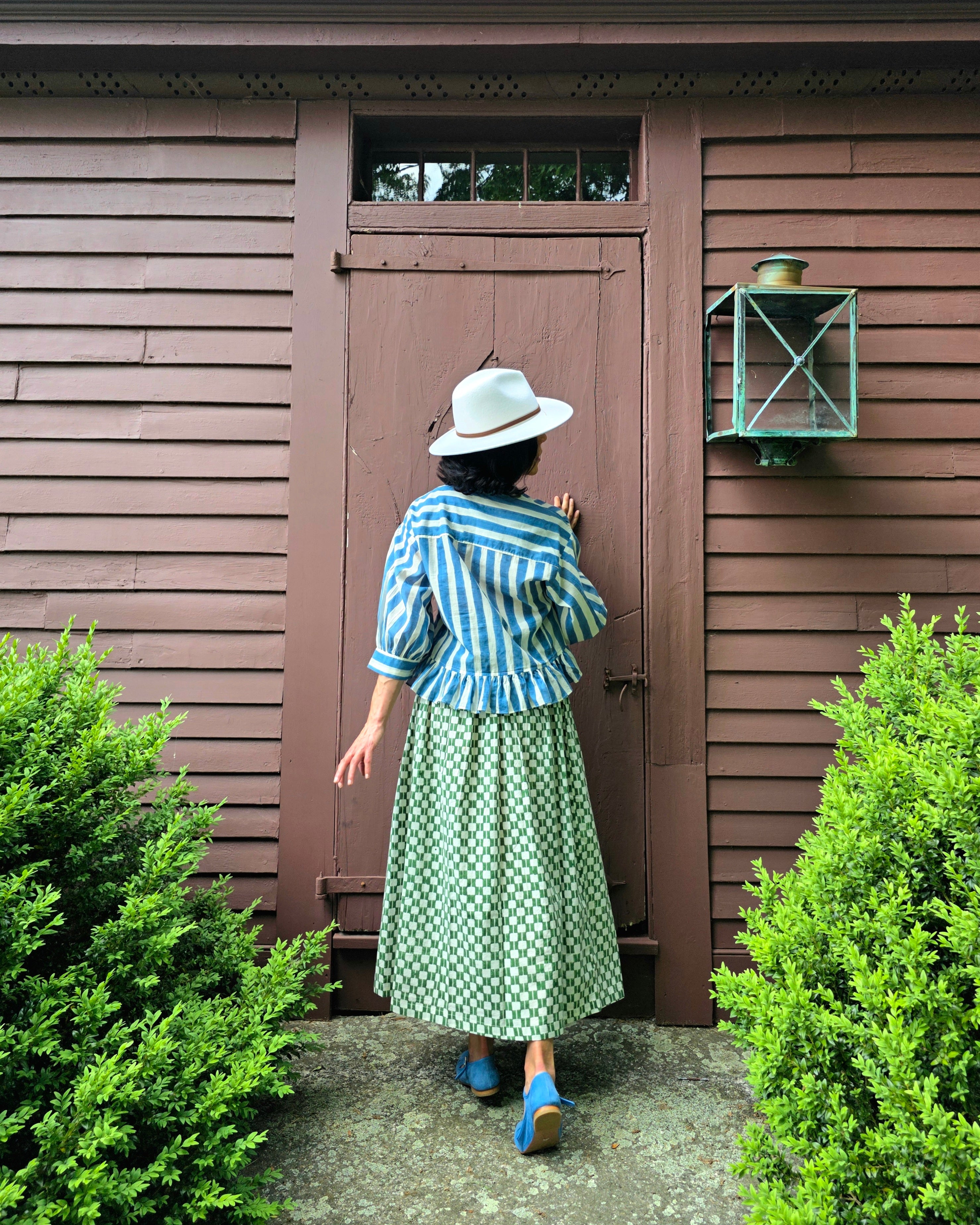 Handwoven blue and white striped cotton top featuring a V-neckline, button-down front, and gathered peplum hem. Made from breathable organic cotton with natural dyes, this lightweight blouse offers a relaxed fit with full sleeves—perfect for summer and resort wear.