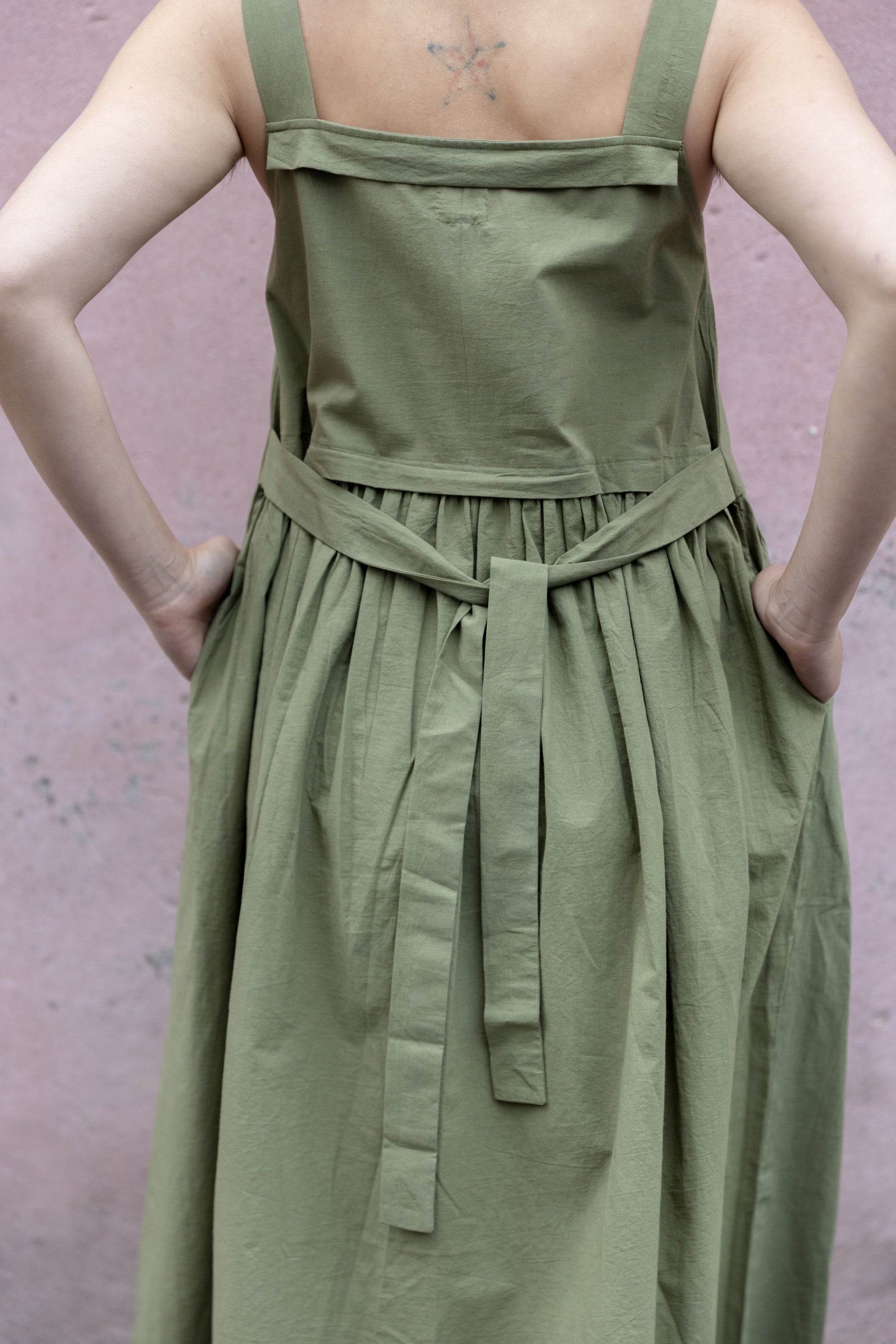 Olive green babydoll midi dress with wide shoulder straps. Features a gathered waistline and a voluminous, flowy skirt. Made from lightweight, structured fabric for a relaxed yet chic look.