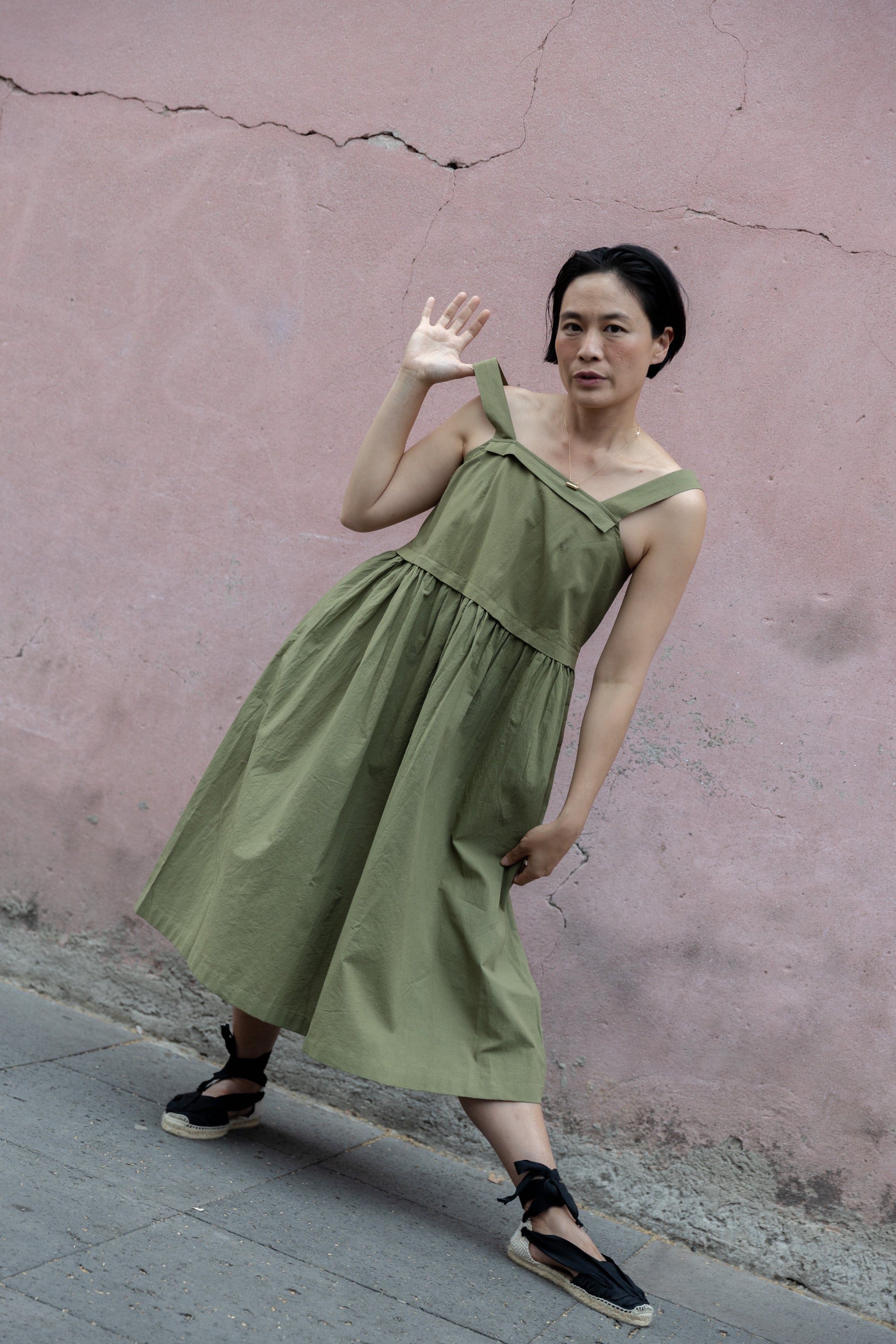 Olive green babydoll midi dress with wide shoulder straps. Features a gathered waistline and a voluminous, flowy skirt. Made from lightweight, structured fabric for a relaxed yet chic look.