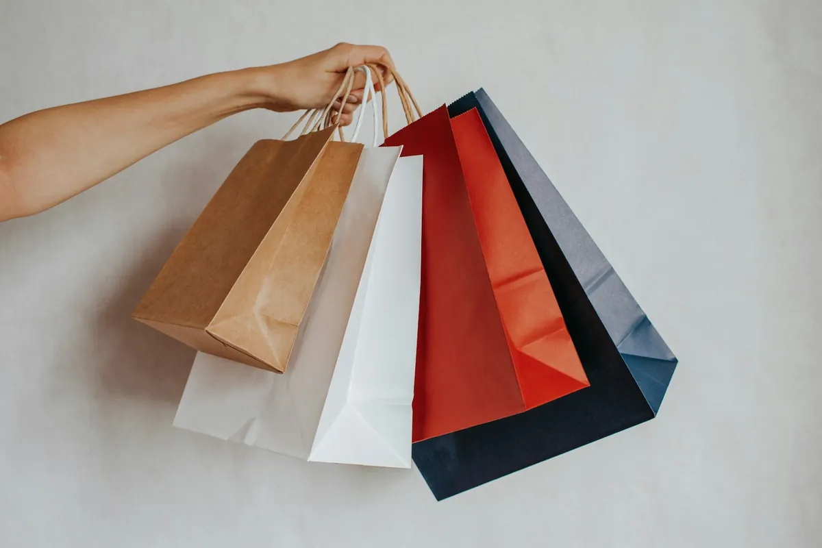 A hand holding colourful shopping bags against a light background