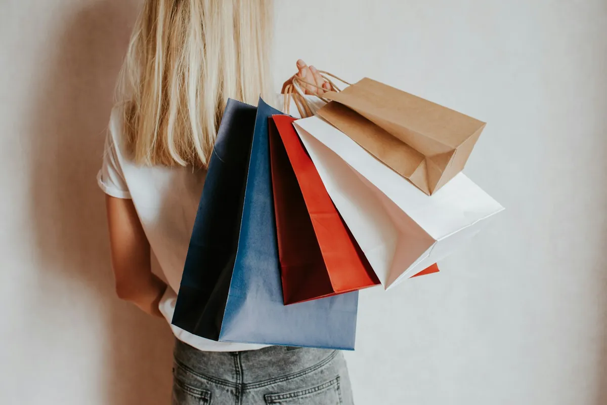 A woman holding colourful shopping bags against a wall