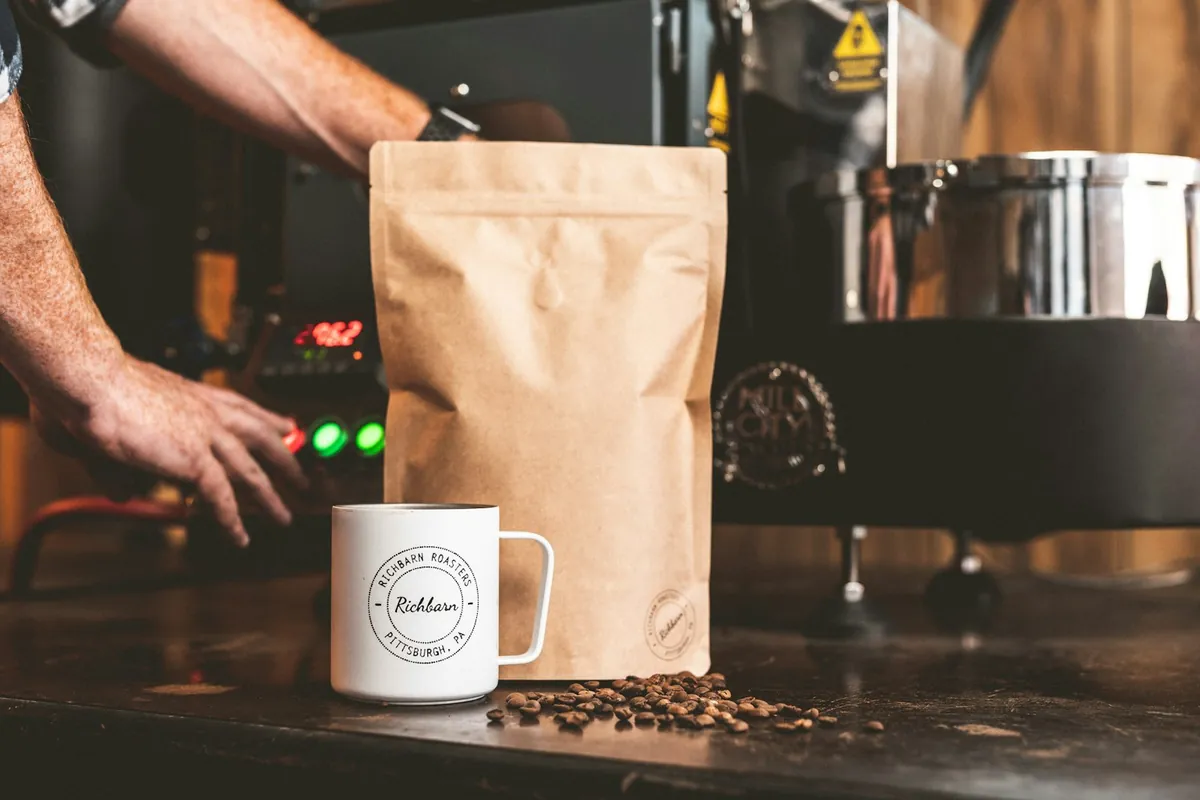 A barista filling a coffee bag beside a mug