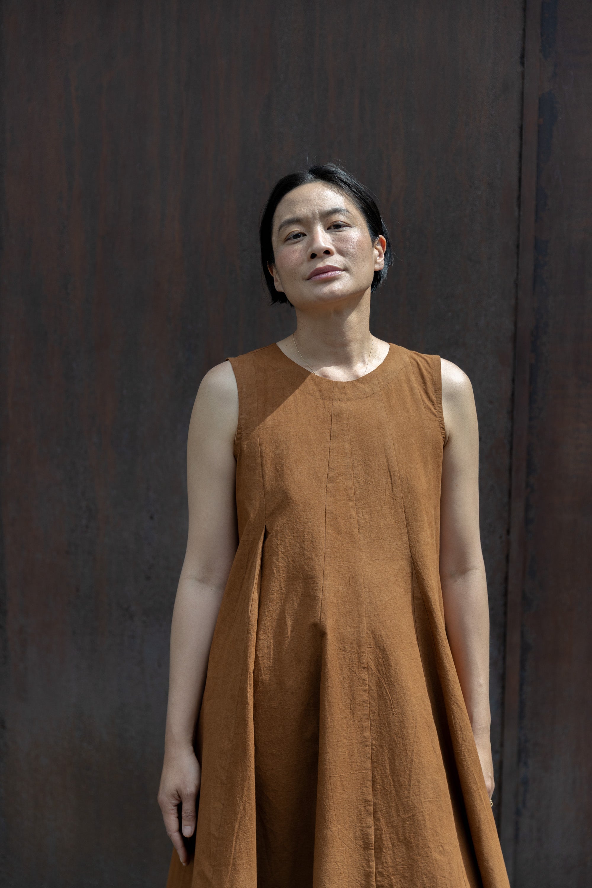 Sleeveless caramel-brown A-line midi dress with a high, round neckline. Features a voluminous flared silhouette, creating a breezy and effortless look. Made from textured, lightweight fabric for a natural, flowy drape.