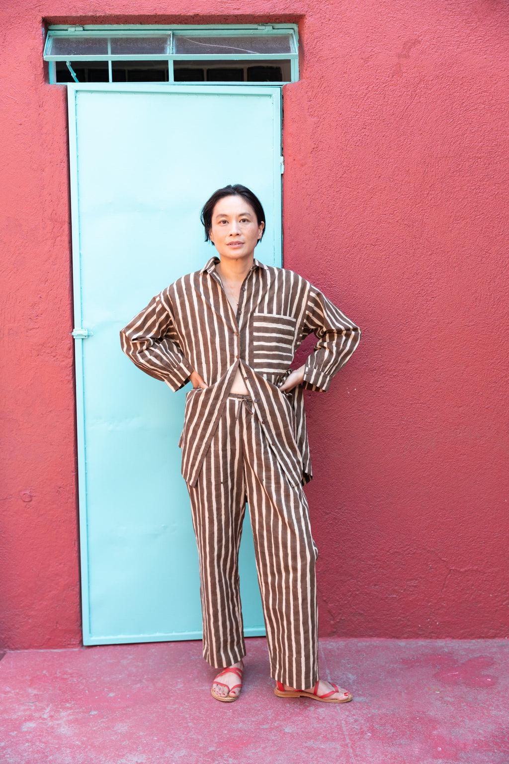 Brown and white vertically striped wide-leg pants with a relaxed, flowy fit. The high-waisted design offers a comfortable and effortless silhouette. The lightweight fabric drapes naturally, making the pants ideal for casual or lounge wear. The bold stripe pattern elongates the legs, adding a stylish touch to the relaxed aesthetic.