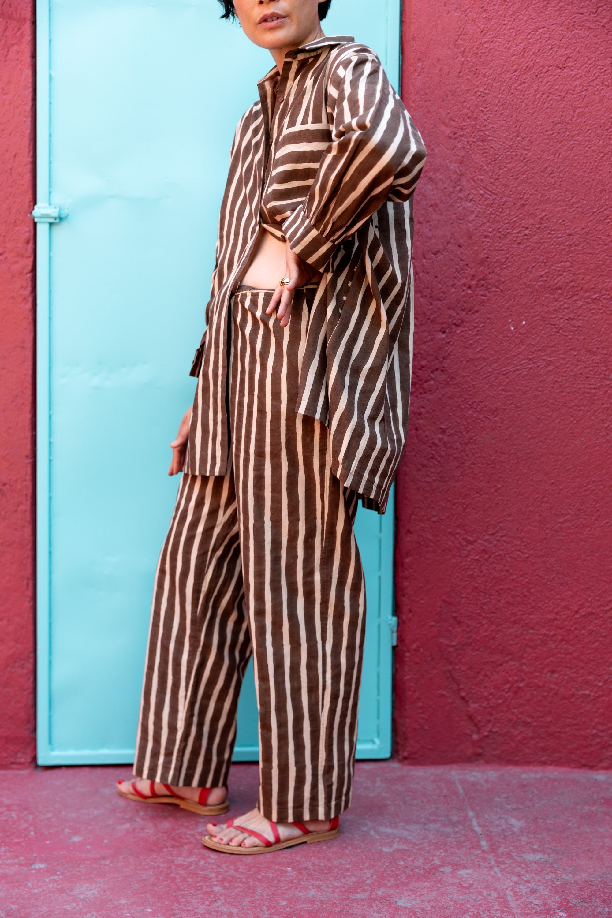 Brown and white vertically striped wide-leg pants with a relaxed, flowy fit. The high-waisted design offers a comfortable and effortless silhouette. The lightweight fabric drapes naturally, making the pants ideal for casual or lounge wear. The bold stripe pattern elongates the legs, adding a stylish touch to the relaxed aesthetic.