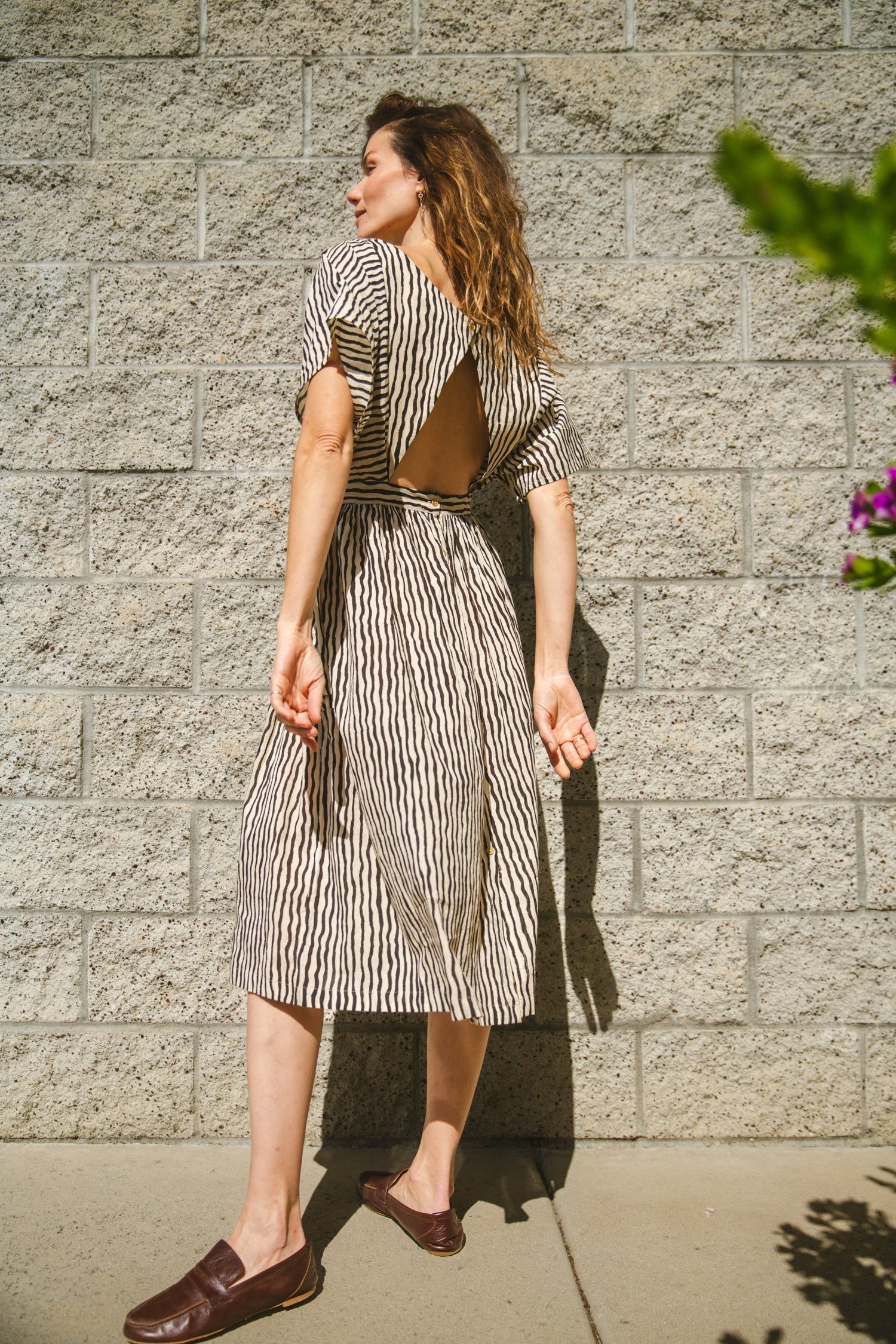 Black and white striped midi dress with short sleeves and an open-back design. Features a cinched waist with a tie detail for a flattering silhouette. Made from lightweight, breathable fabric, perfect for warm weather. A stylish choice for casual and semi-formal occasions.