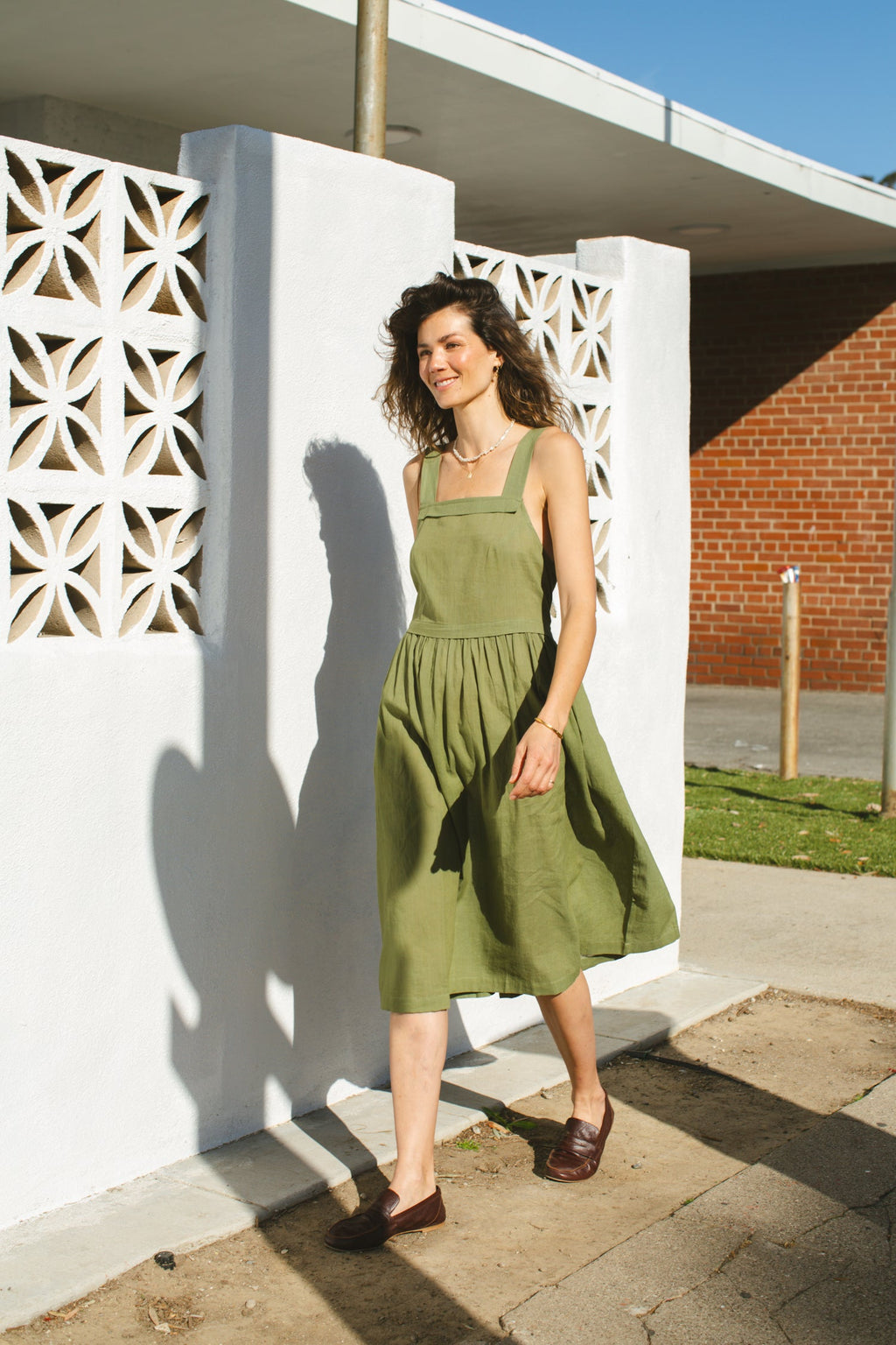 Olive green babydoll midi dress with wide shoulder straps. Features a gathered waistline and a voluminous, flowy skirt. Made from lightweight, structured fabric for a relaxed yet chic look.