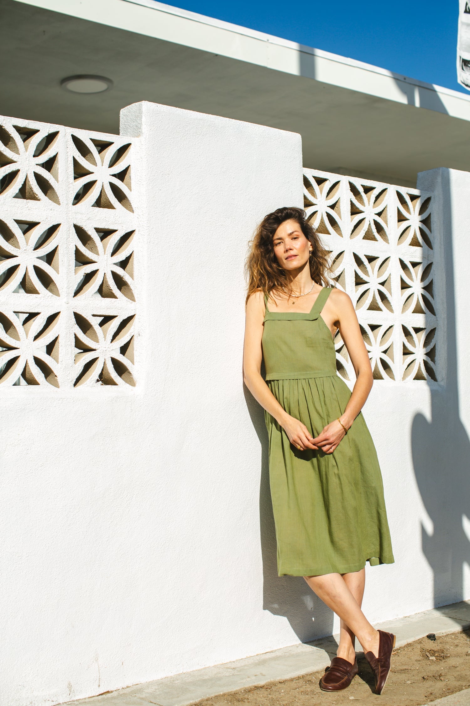 Olive green babydoll midi dress with wide shoulder straps. Features a gathered waistline and a voluminous, flowy skirt. Made from lightweight, structured fabric for a relaxed yet chic look.