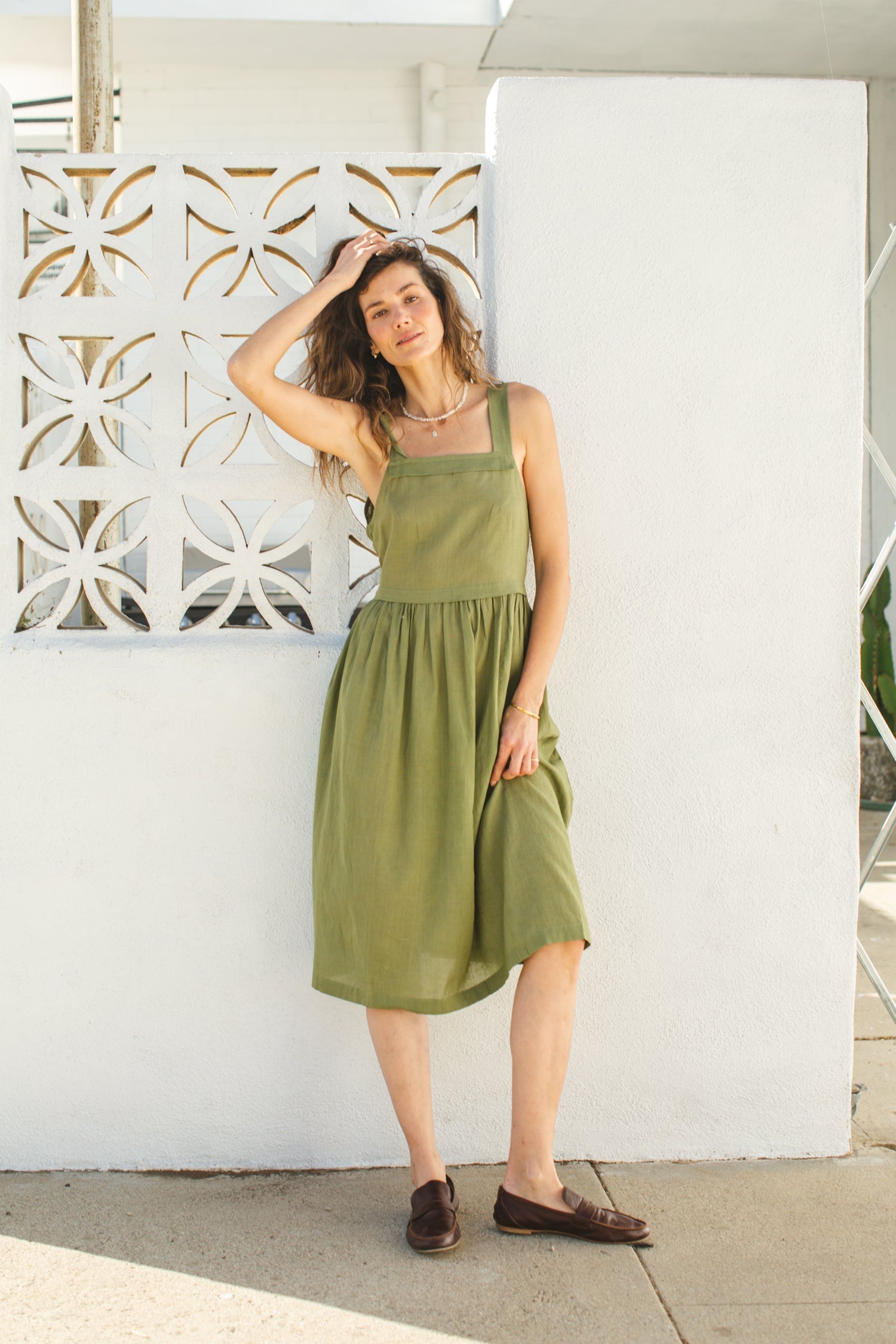 Olive green babydoll midi dress with wide shoulder straps. Features a gathered waistline and a voluminous, flowy skirt. Made from lightweight, structured fabric for a relaxed yet chic look.