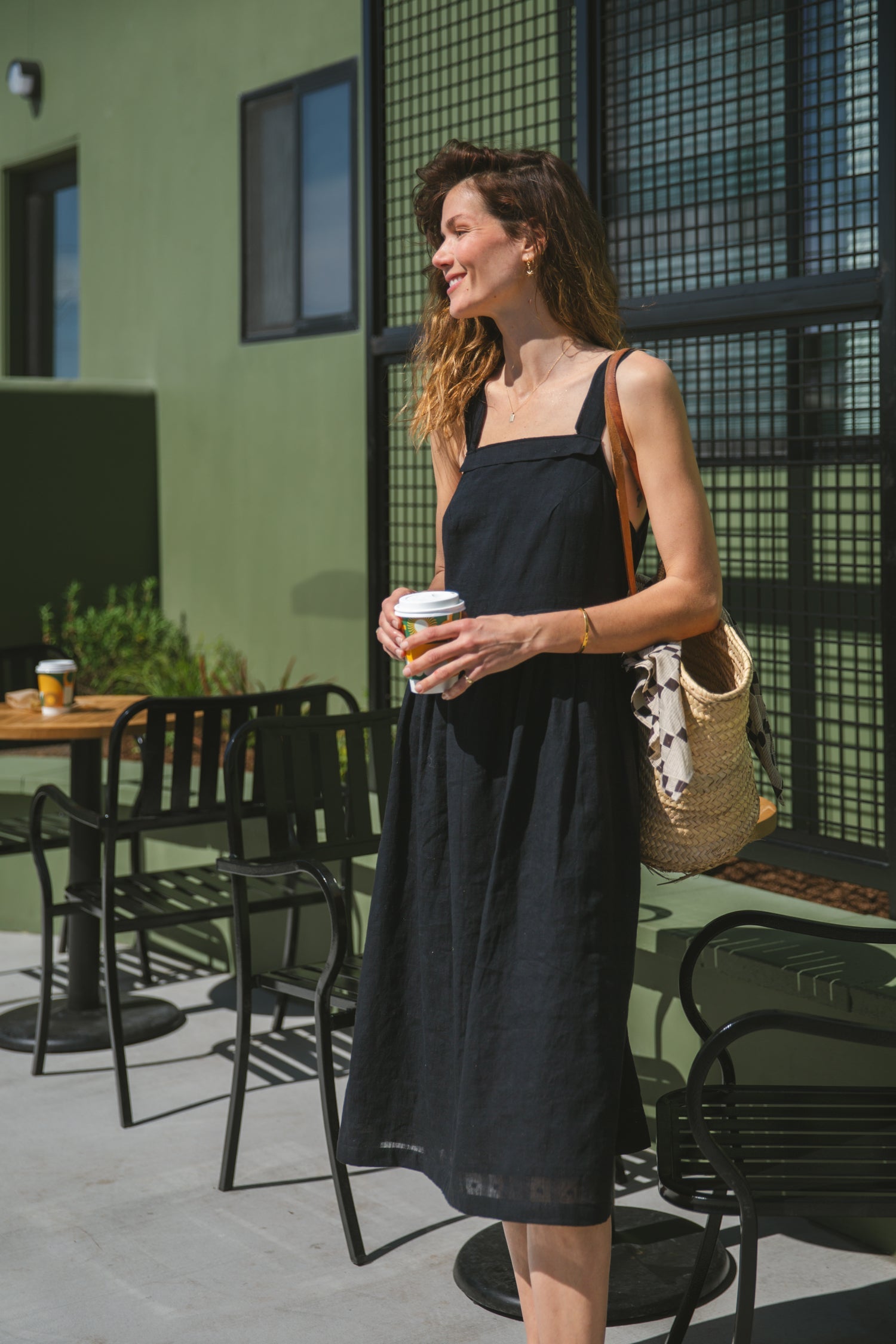 This is a black sleeveless midi dress with a structured square neckline and wide shoulder straps. The dress features a loose, flowing silhouette with a gathered waistline that adds volume and movement. Crafted from a lightweight, breathable fabric, it drapes effortlessly, making it perfect for warm weather. Functional side pockets enhance its practicality, while the relaxed fit exudes a laid-back yet refined charm. The minimalist design and deep black hue create a versatile piece that can be styled casually