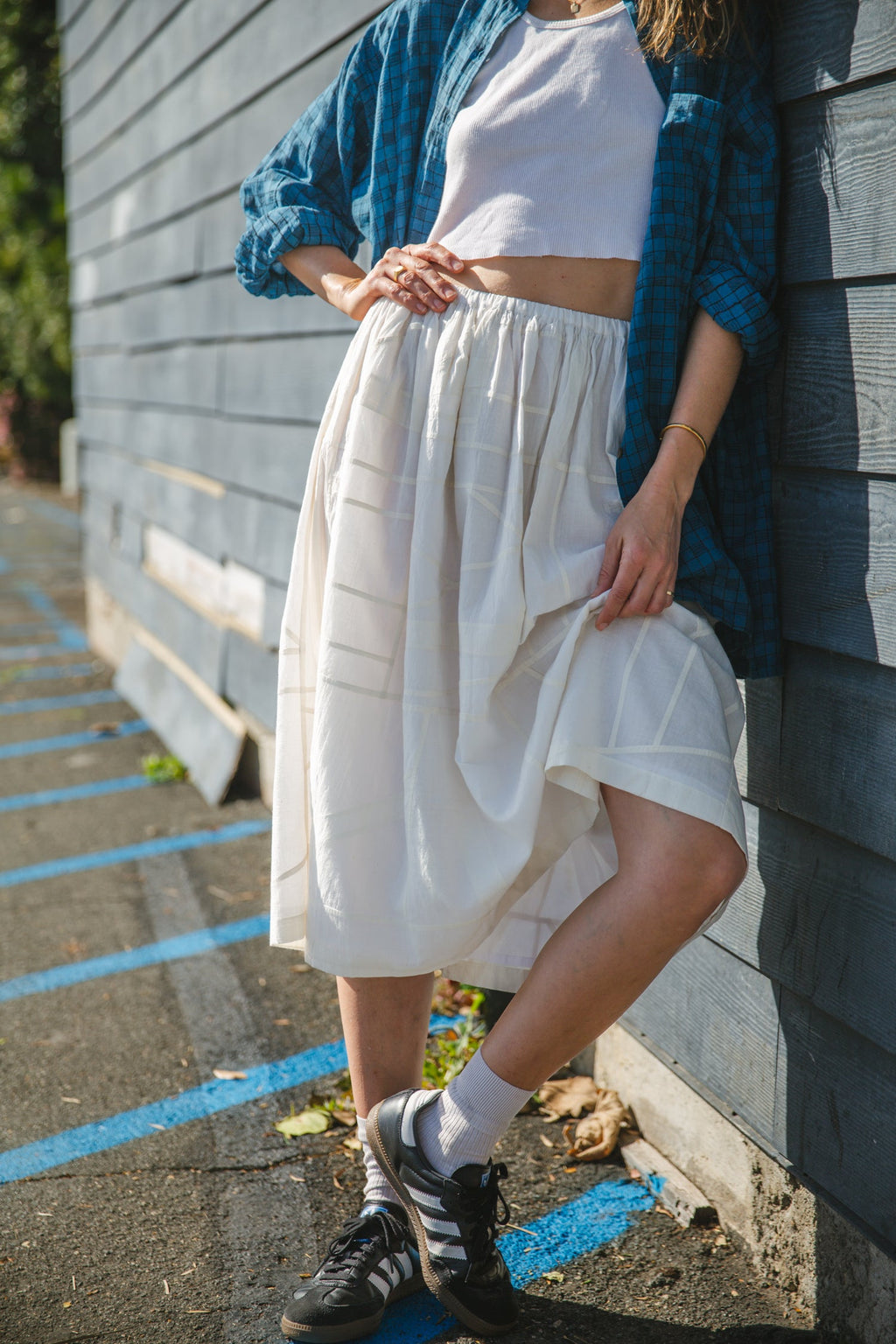 White flowy midi skirt with subtle plaid pattern, lightweight fabric, and gathered waist for an elegant and casual look.