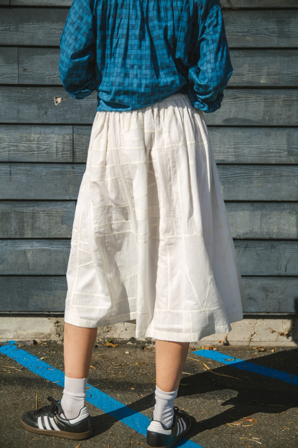 White flowy midi skirt with subtle plaid pattern, lightweight fabric, and gathered waist for an elegant and casual look.
