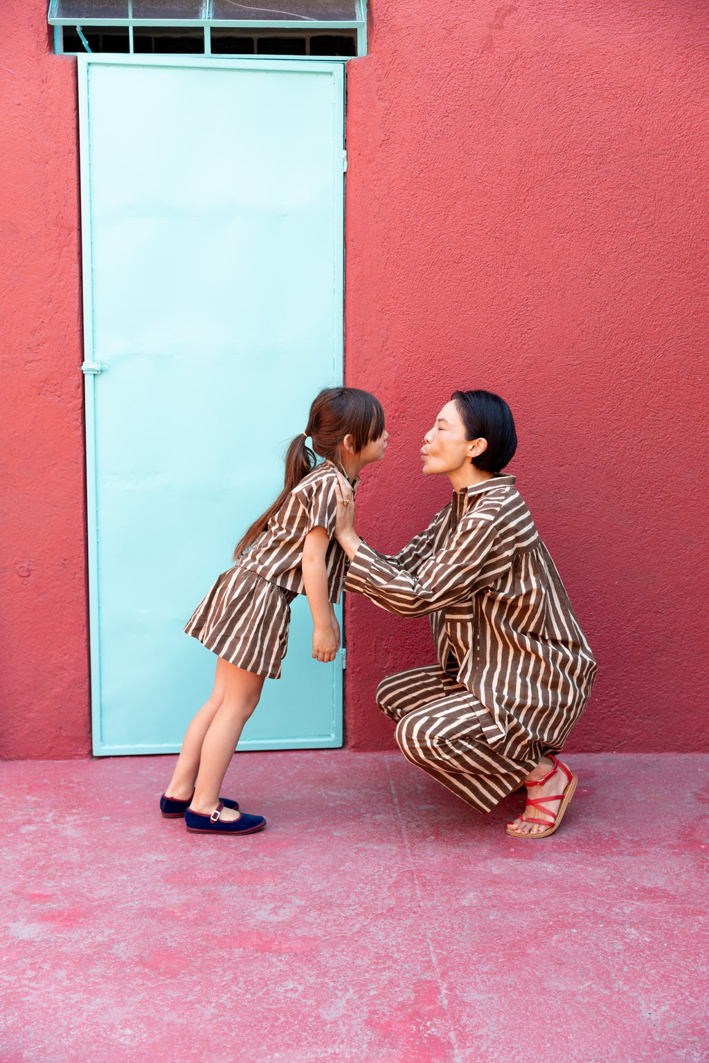 A pair of brown and white vertically striped kids' shorts with a loose, relaxed fit. The shorts have an elastic waistband for comfort and a slightly flared silhouette, styled as part of a matching set with a collared short-sleeve shirt.