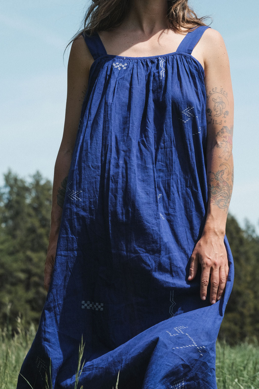 Long indigo blue Jamdani dress featuring wide straps, a gathered neckline, and subtle white abstract geometric motifs. Handwoven from soft, lightweight cotton and dyed with azo-free dyes, this fully lined dress is crafted over 7 days using traditional weaving techniques. Ethically made with a relaxed, bohemian silhouette, it's perfect for summer wear—combining artisanal charm with breathable comfort.