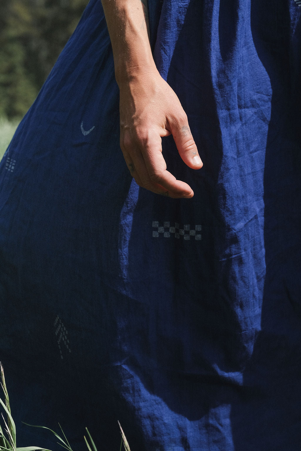 Long indigo blue Jamdani dress featuring wide straps, a gathered neckline, and subtle white abstract geometric motifs. Handwoven from soft, lightweight cotton and dyed with azo-free dyes, this fully lined dress is crafted over 7 days using traditional weaving techniques. Ethically made with a relaxed, bohemian silhouette, it's perfect for summer wear—combining artisanal charm with breathable comfort.