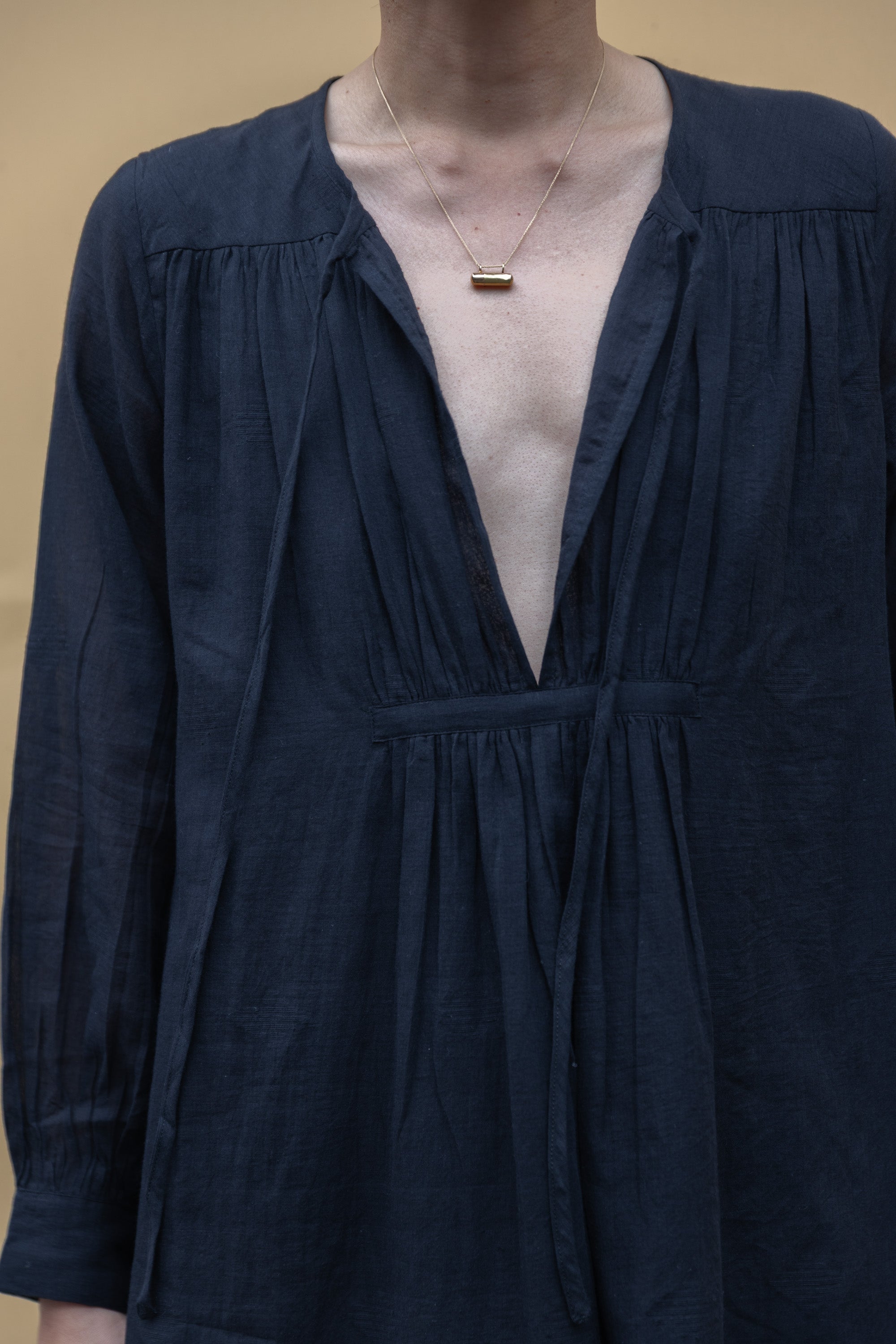 Black midi dress with long sleeves, a deep V-neckline with delicate gathers, and adjustable tie details. Designed with a relaxed waist and flowy fabric for effortless movement.