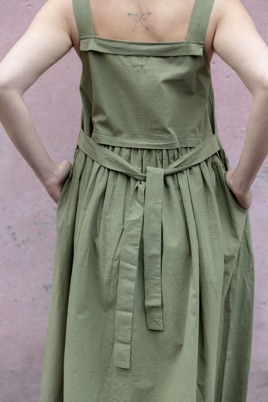 Olive green babydoll midi dress with wide shoulder straps. Features a gathered waistline and a voluminous, flowy skirt. Made from lightweight, structured fabric for a relaxed yet chic look.